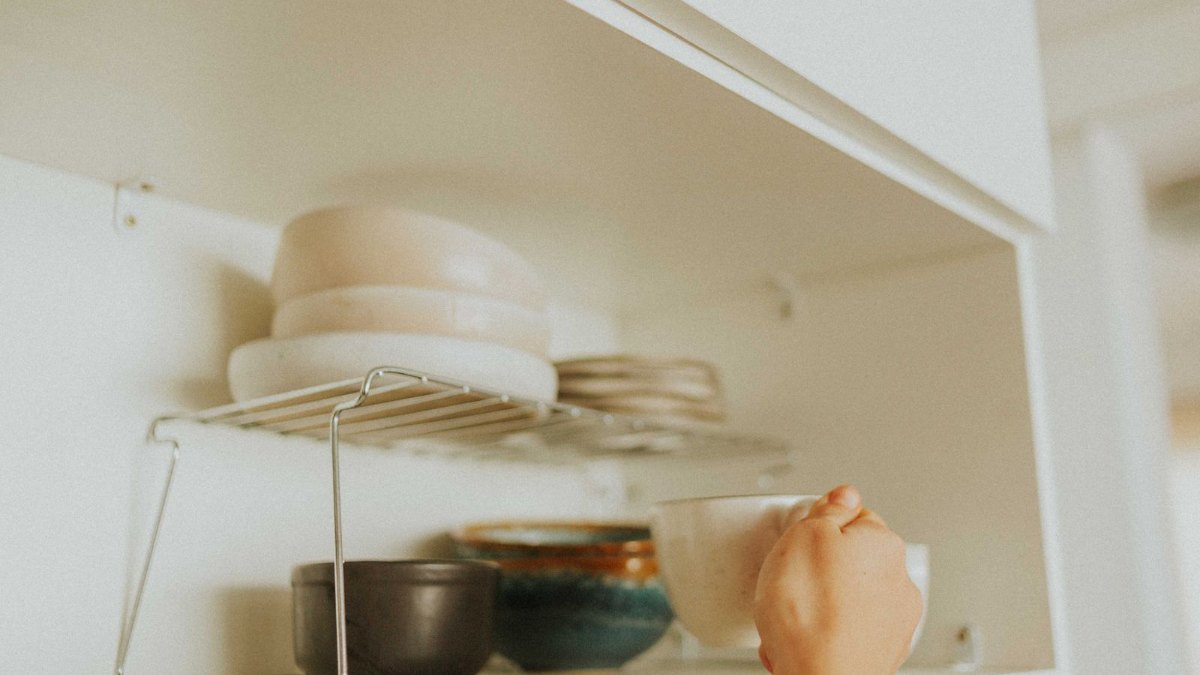reaching into a kitchen cabinet of mugs while decluttering