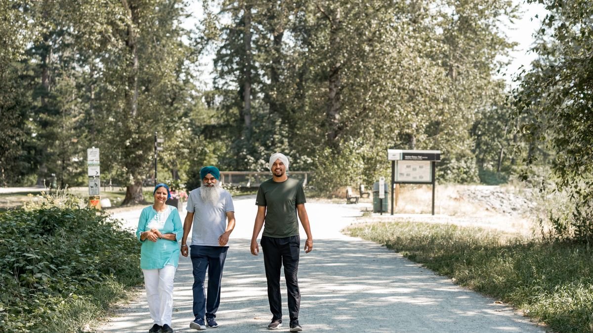 three family members walking together on a tree-lined park path